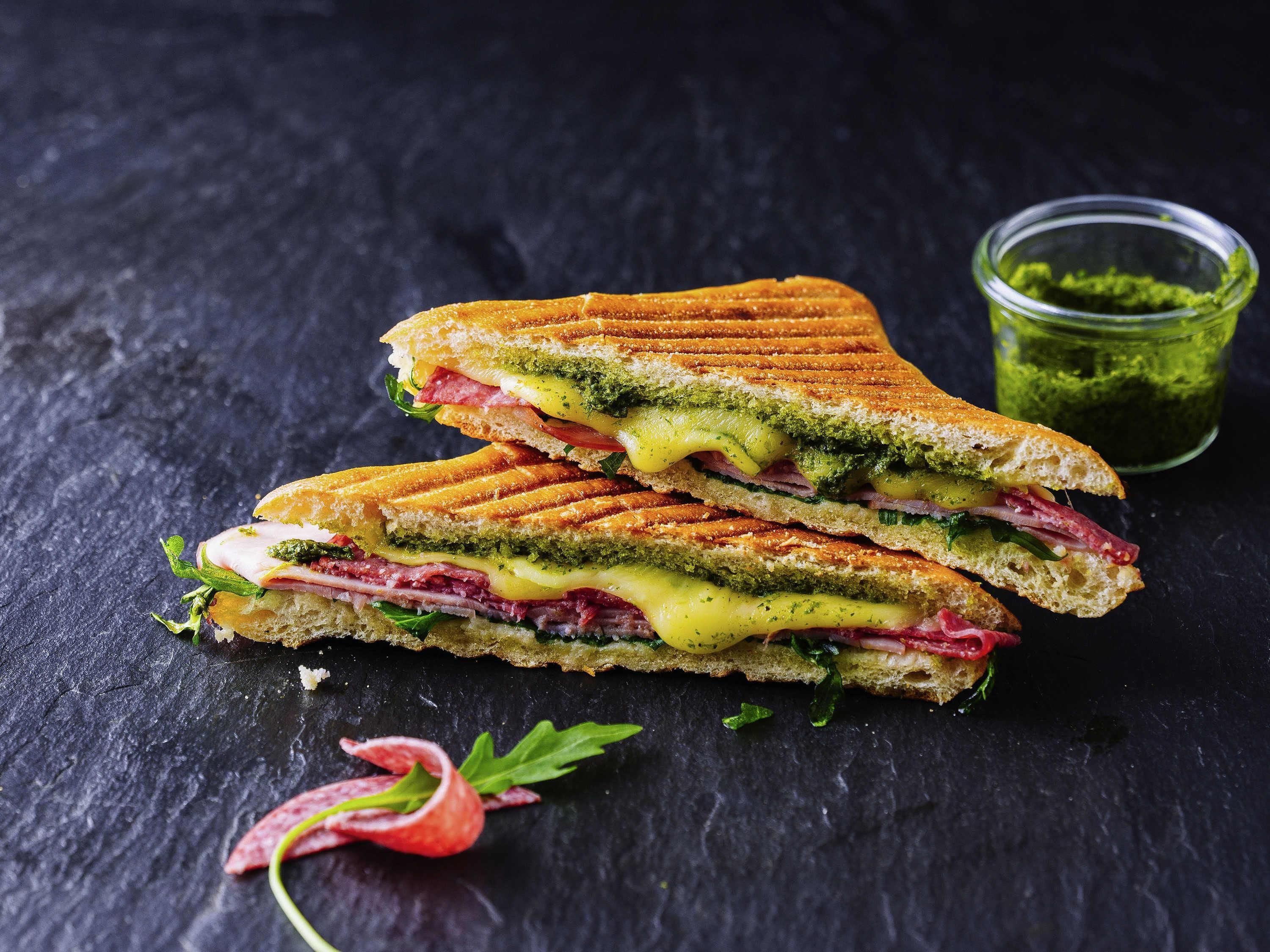A sandwich with multiple layers, including greens, cheese, and meat, on a dark surface.