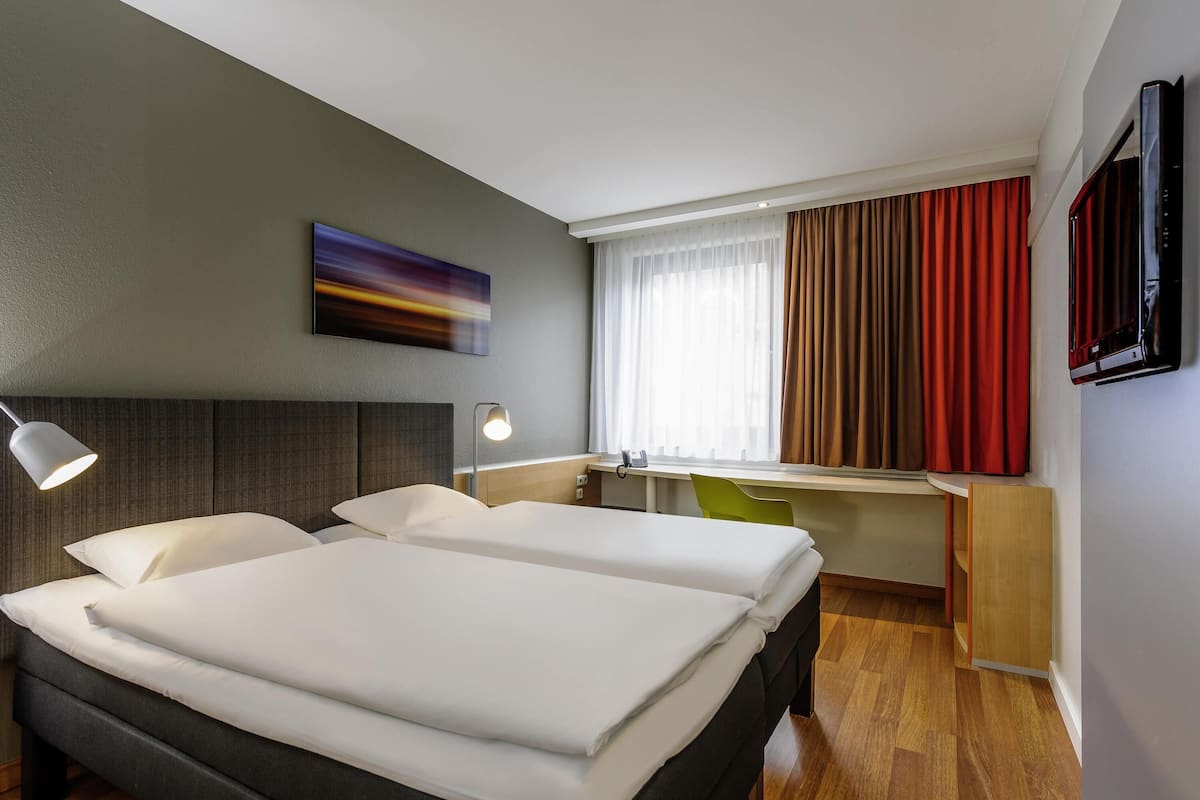 Une chambre d’hôtel avec deux lits, un bureau, une chaise, une télévision et un tableau au mur.