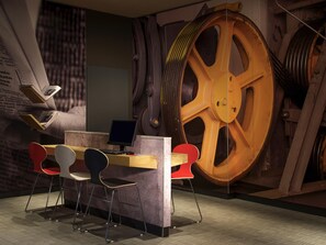Ein Zimmer mit Schreibtisch, zwei Stühlen, einem Computer und einem großen Funktionsrad im Hintergrund.
