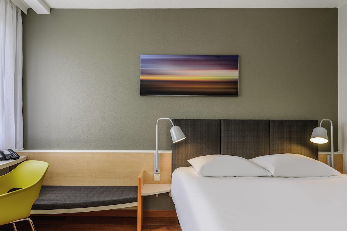 Una habitación de hotel con cama, lámparas de noche, escritorio y una silla.