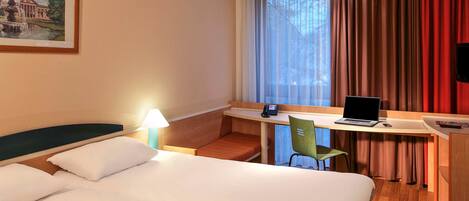 Una habitación de hotel con una cama, un escritorio con una computadora portátil, un teléfono y una silla.