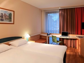 Une chambre d’hôtel avec un lit, un bureau équipé d’un ordinateur portable, un téléphone et une chaise.