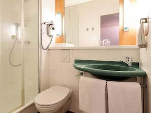 Ein Badezimmer mit Duschkabine aus Glas, einer weißen Toilette, einem grünen Waschbecken und einem Spiegel mit Holzrahmen.
