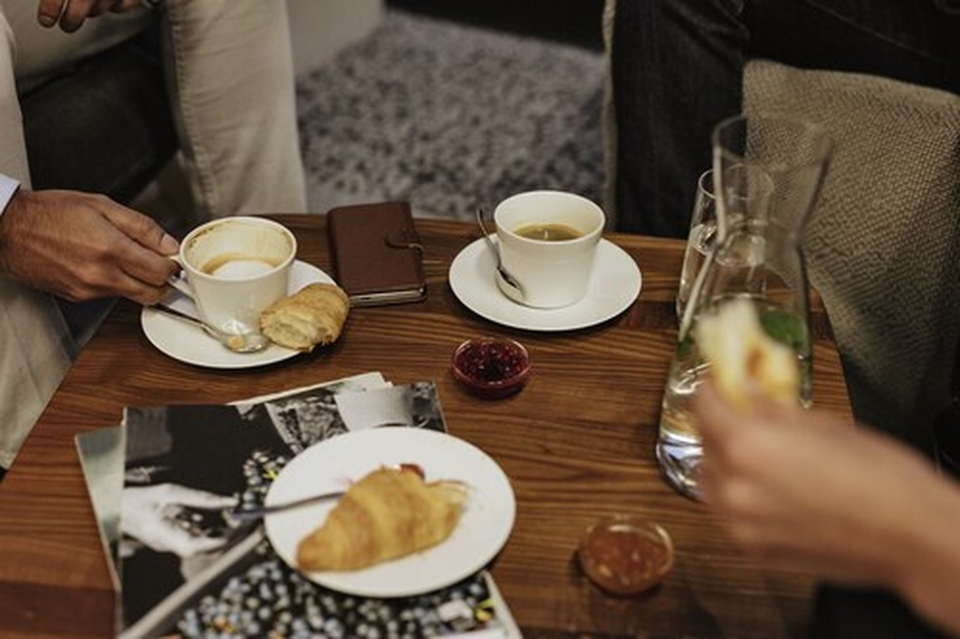 Una mesa de comedor con un croissant, una taza de café, un vaso de agua y un recipiente pequeño de mermelada.
