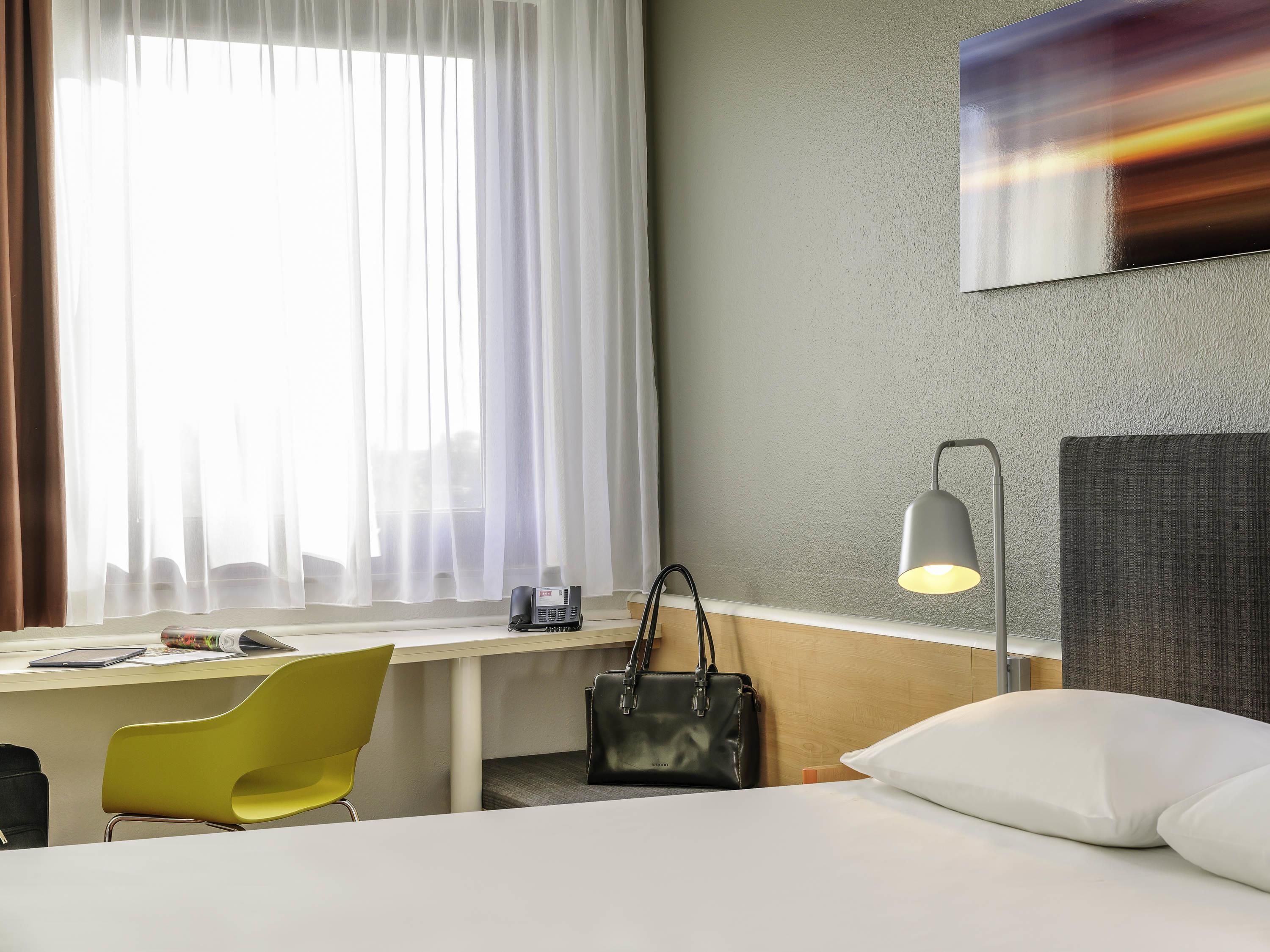 Habitación de hotel con cama, escritorio, silla, lámpara y un cuadro en la pared.