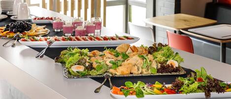 Una mesa de buffet con diversos platos, entre ellos ensaladas, carnes y una bandeja de frutas.