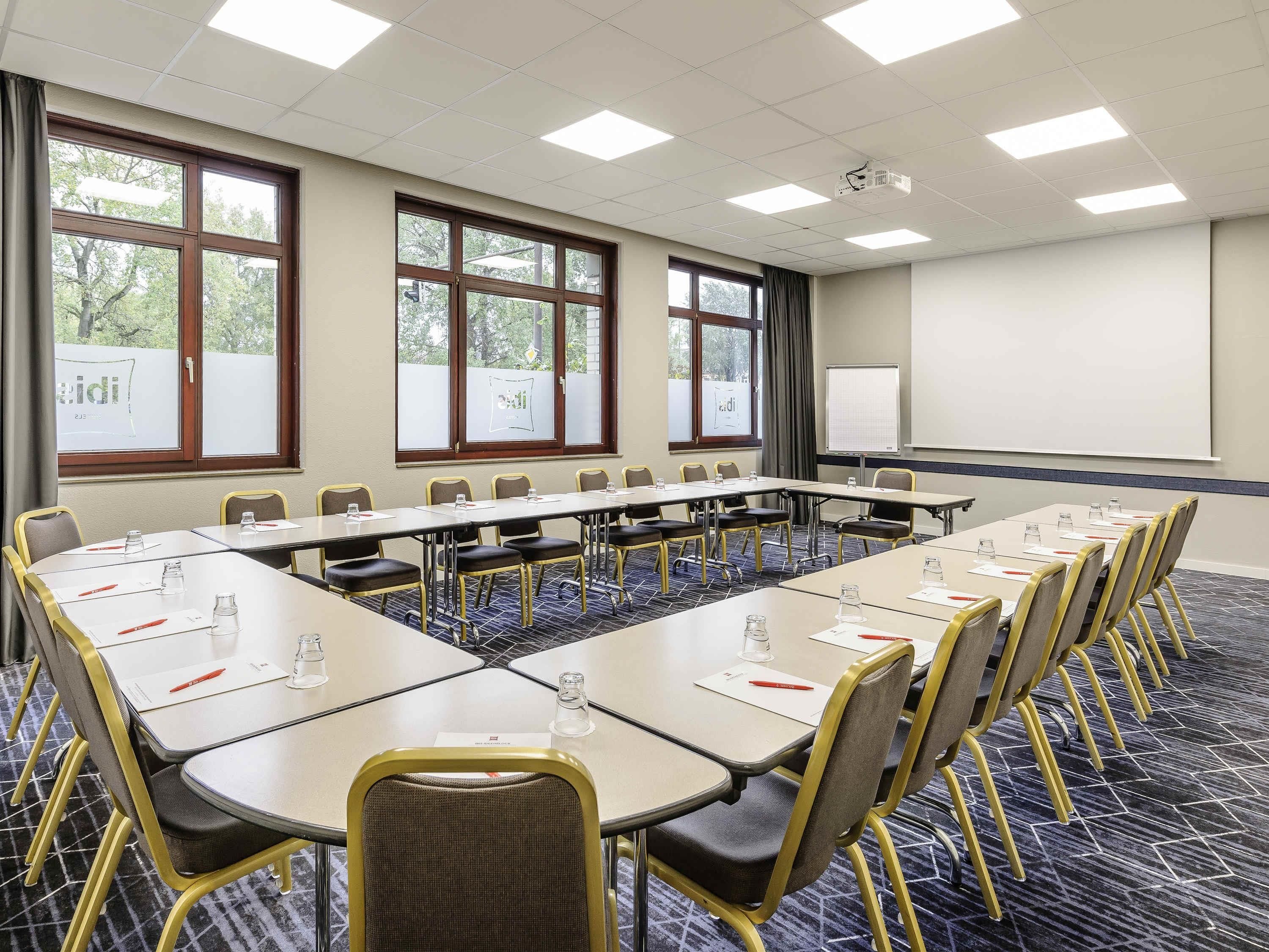 A conference room with long tables, chairs, a projector, and a whiteboard.