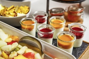 Eine Dessertplatte mit verschiedenen kleinen Gläsern Custard und Fruchtkompott, sowie eine Schale, die gebratenen Kochbananen zu sein scheint.