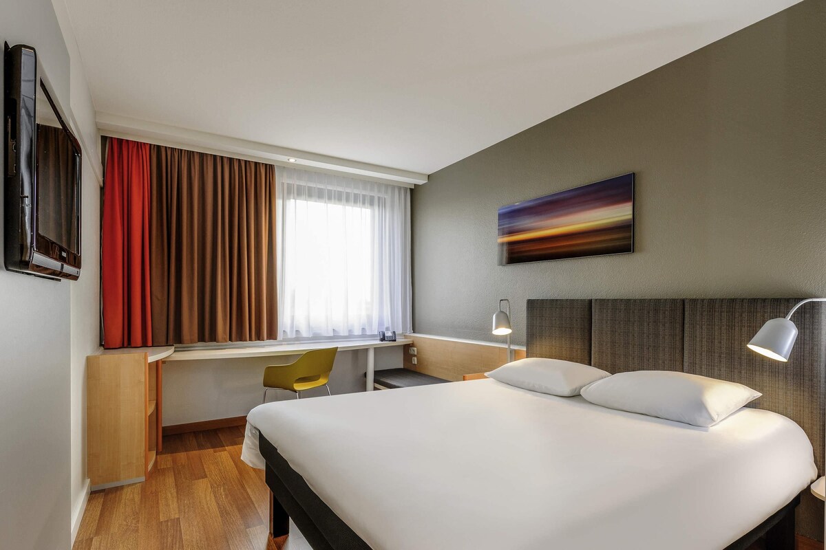 Ein Hotelzimmer mit Bett, Schreibtisch, Stuhl und Fernseher.