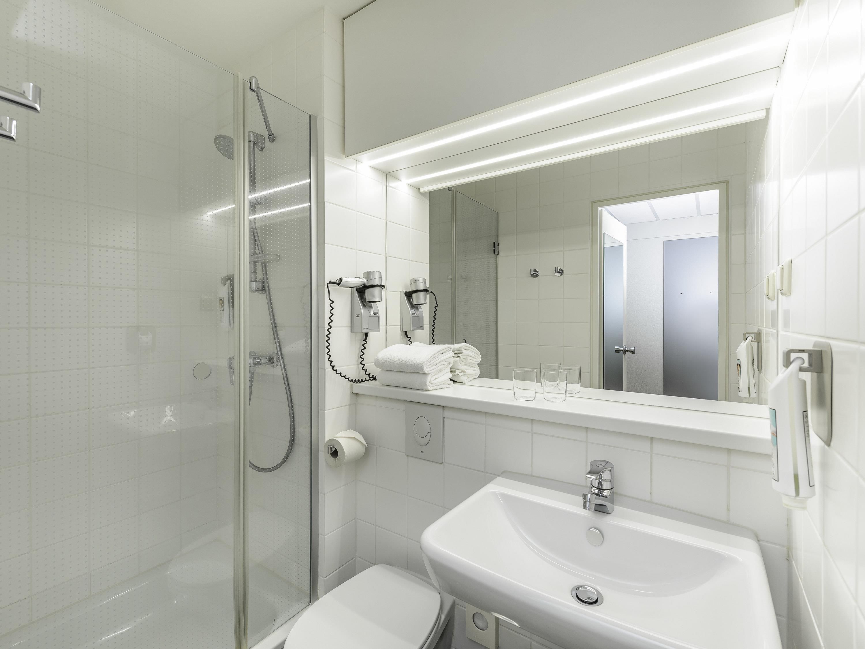 Un baño moderno con ducha envuelta en vidrio, un lavamanos blanco y un espejo grande.