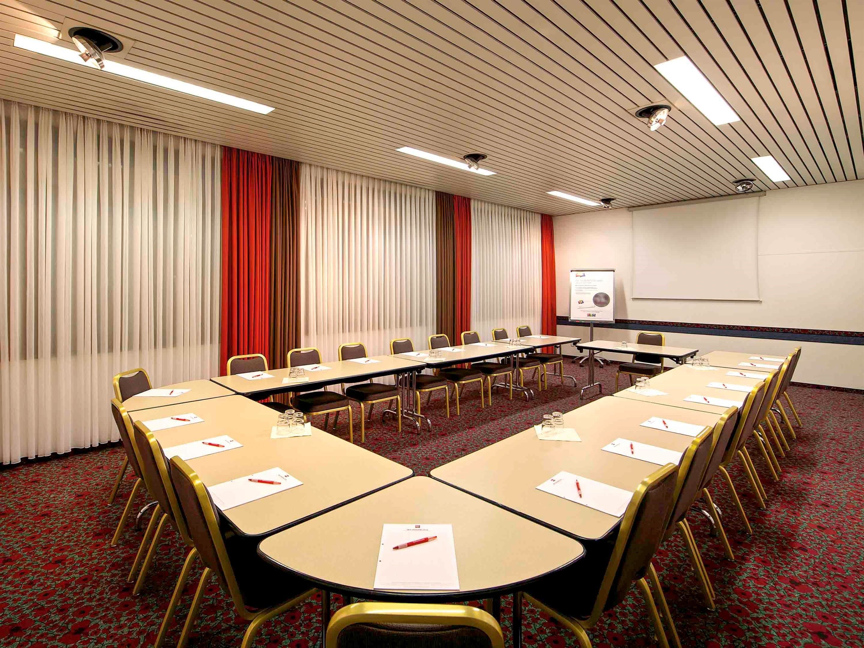 A conference room with a long table, chairs, a projector screen, and a whiteboard.