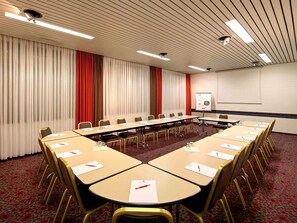 Une salle de conférence équipée d’une longue table, de chaises, d’un écran de projection et d’un tableau blanc.