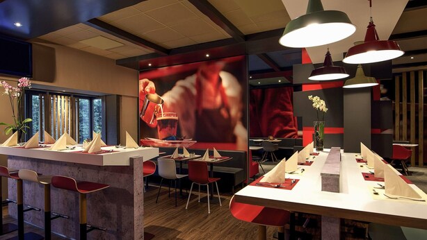 A modern restaurant interior with a bar area, dining tables, and red and white decor. - ibis Bremen City Hotel (Bremen)