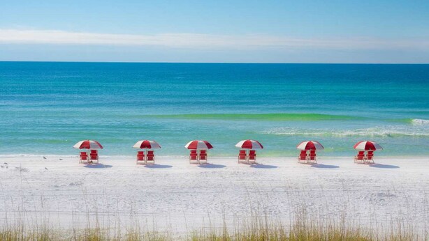 Una playa con cinco sombrillas rojas y blancas y sillas de playa alineadas.