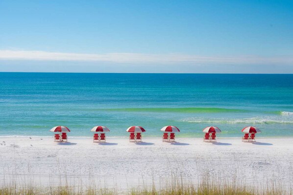 A beach with five red and white umbrellas and beach chairs aligned in a row. - Holiday Inn & Suites Clearwater Beach S-Harbourside by IHG (Indian Rocks Beach)