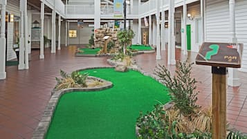 A miniature golf course with artificial turf and rock formations, surrounded by white pillars and a brick floor.