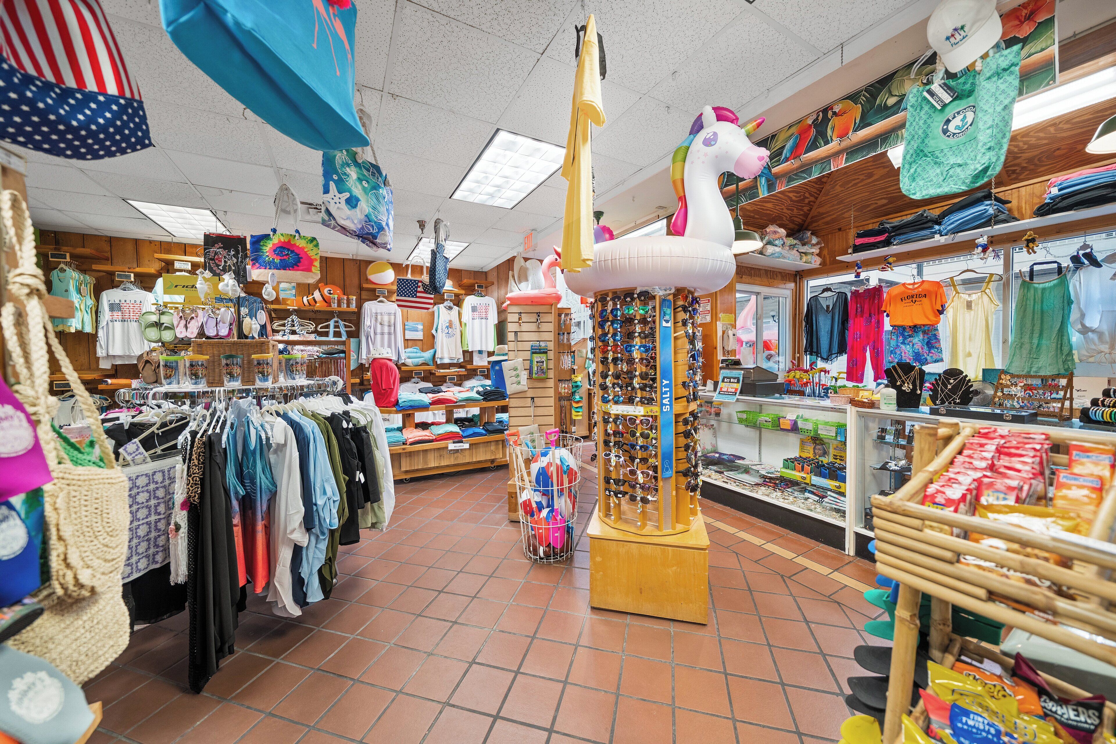 Un magasin de vêtements avec des portants remplis de vêtements, un présentoir de lunettes de soleil et divers articles suspendus.
