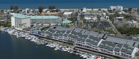 A marina with multiple boats docked, a large hotel with a green roof, and a view of the ocean.