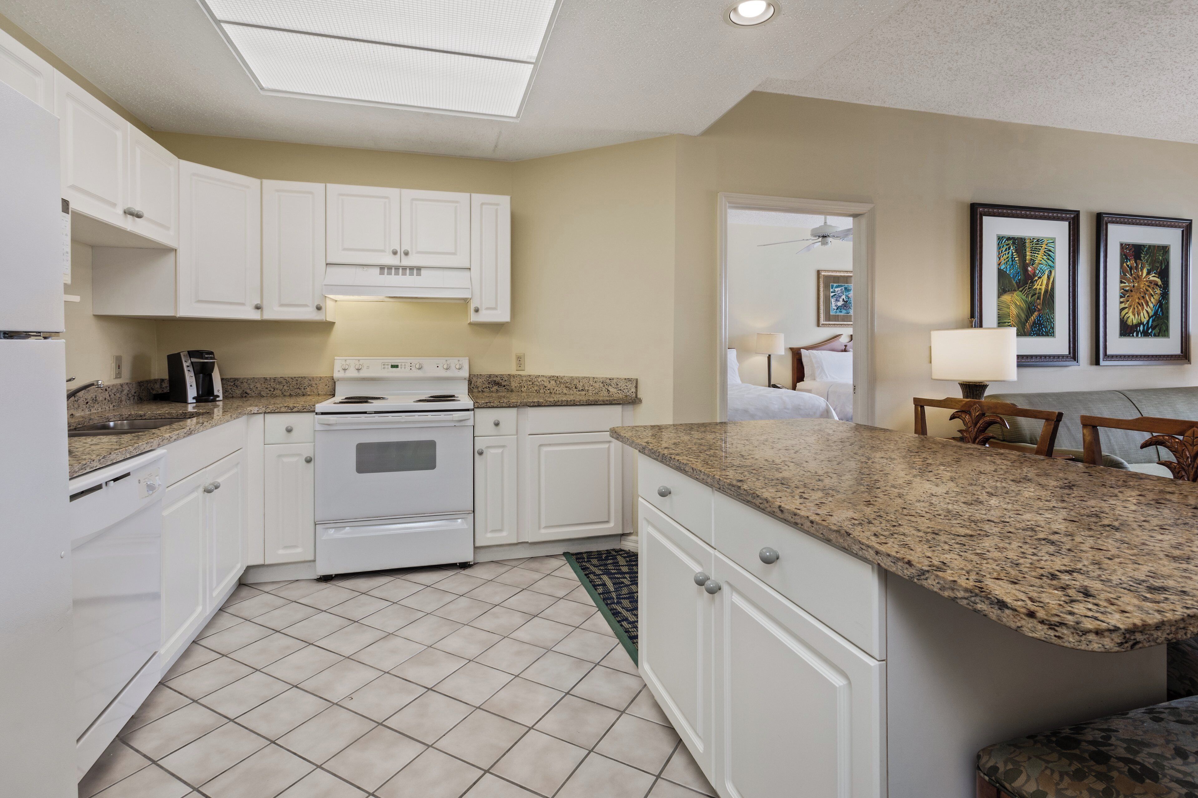 A kitchen with white cabinets, a white stove, granite countertops, and a tiled floor.