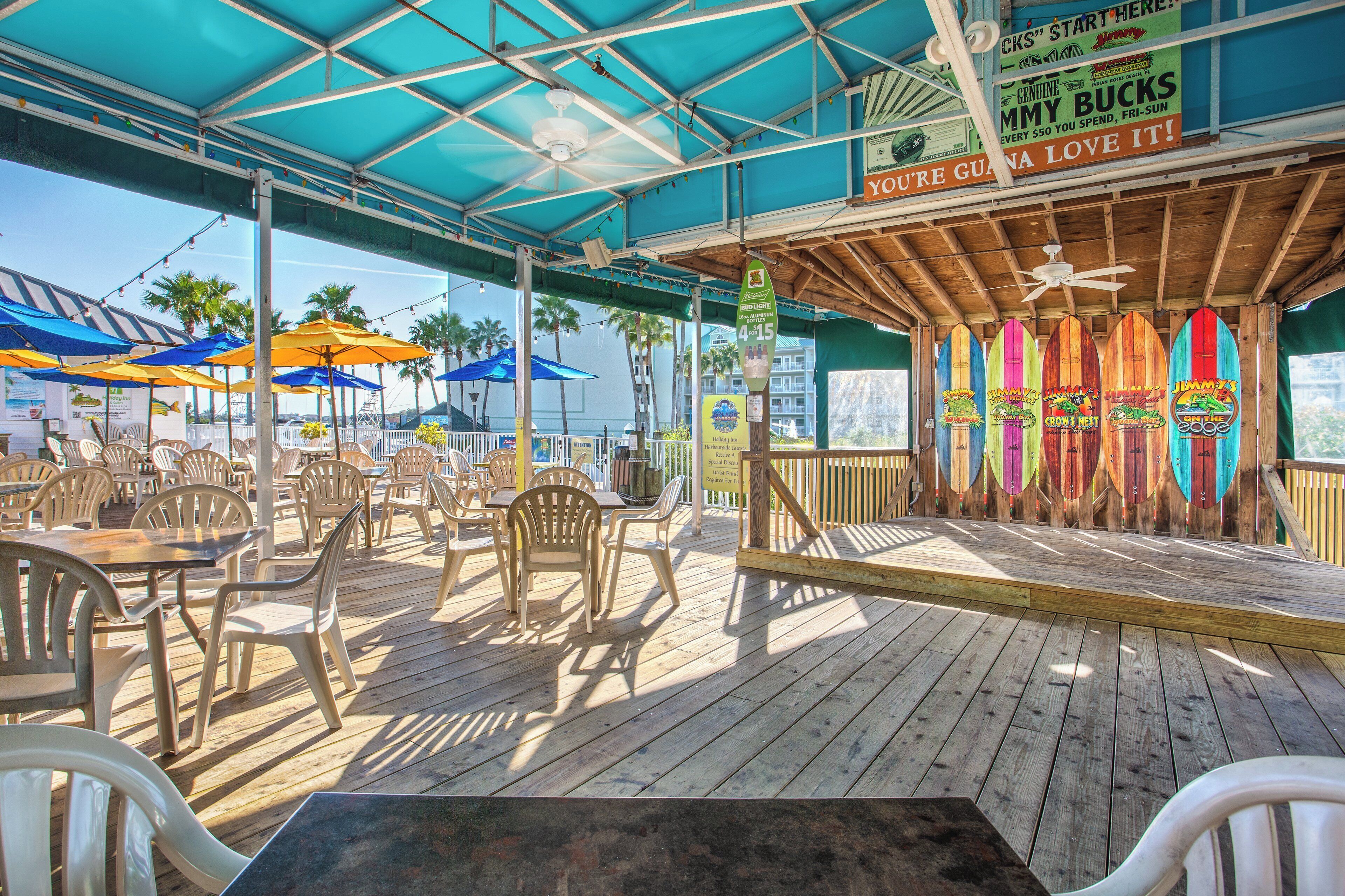 An outdoor dining area with wooden tables and chairs, umbrellas, and surfboards as decorations.