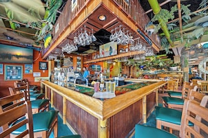 Uma área de bar com mobiliário de madeira, balcão e copos pendurados.