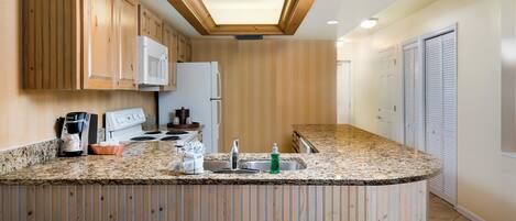 A kitchen with wooden cabinets, a white refrigerator, a stove, and a granite countertop.