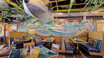 Un restaurante con murales de temática náutica, cabinas de madera y mesas con cojines azules.