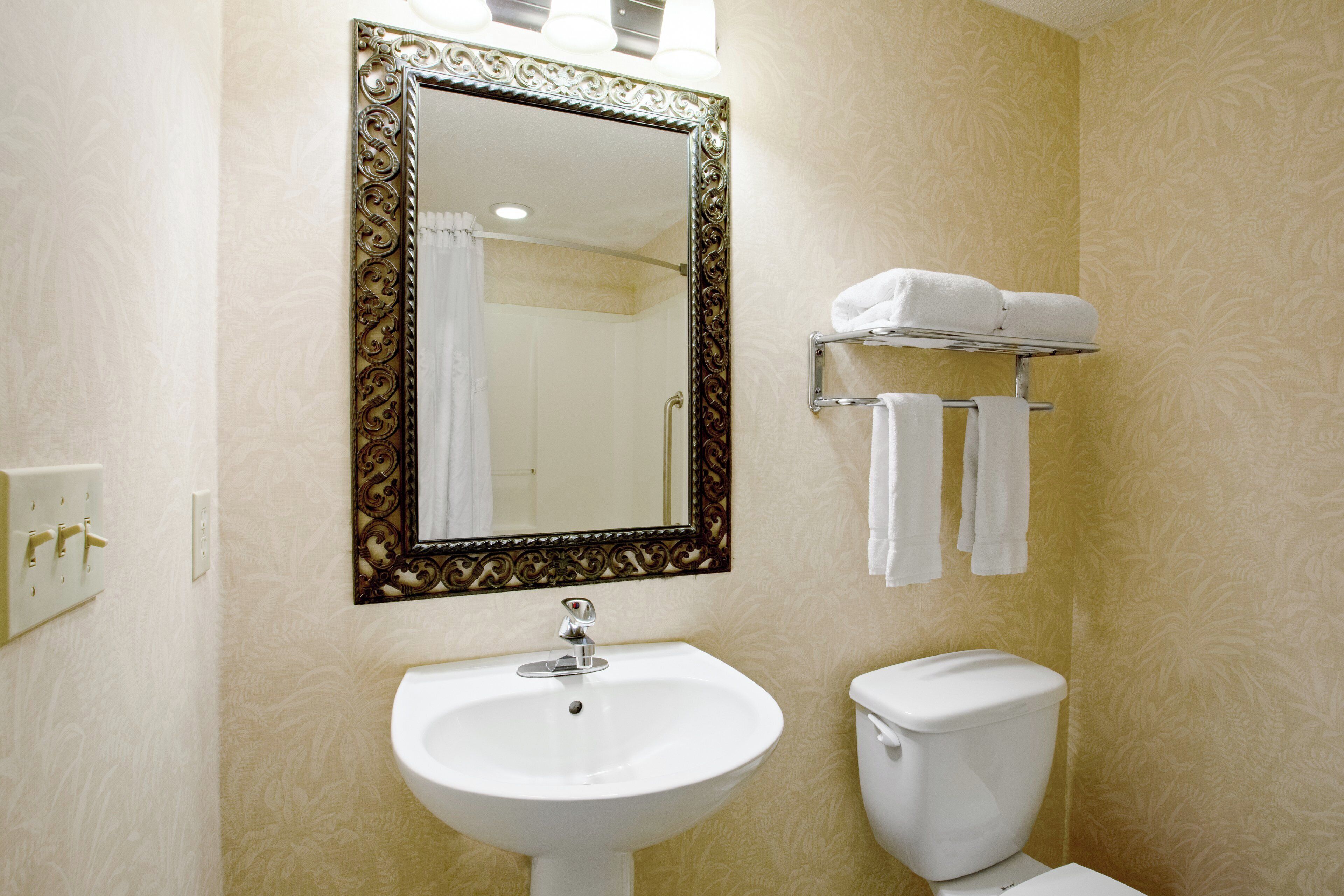 A bathroom with a white sink, a toilet, a mirror with an ornate frame, and a towel rack with towels.