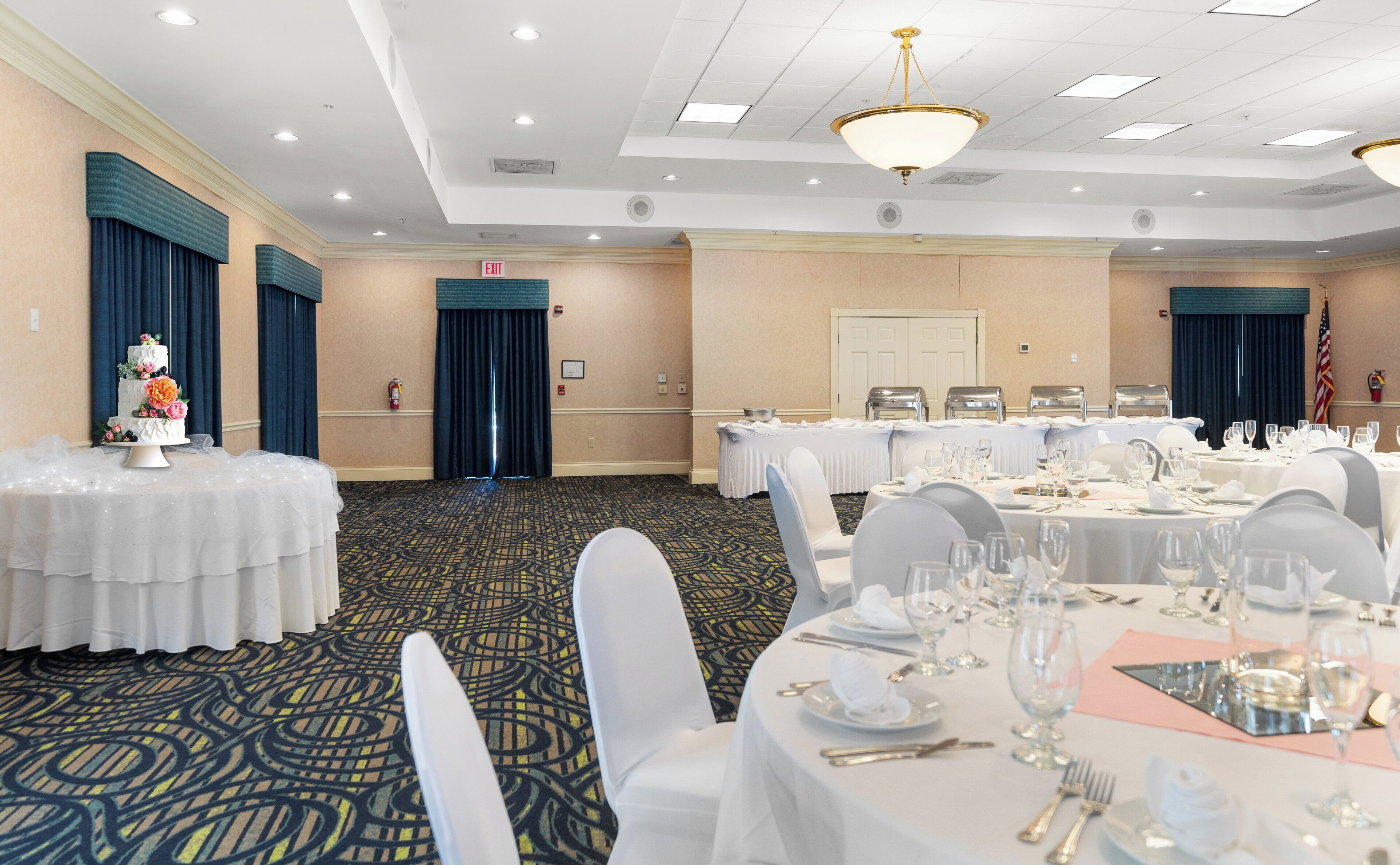 Un salón de banquetes con mesas redondas dispuestas para un evento formal, con manteles blancos, cubiertos y cristalería.
