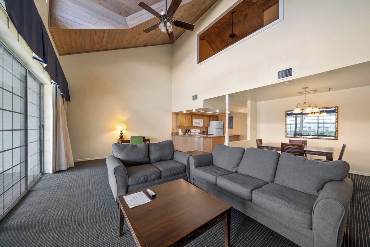 A spacious living area with a large gray sectional sofa, a wooden coffee table, and a ceiling fan.