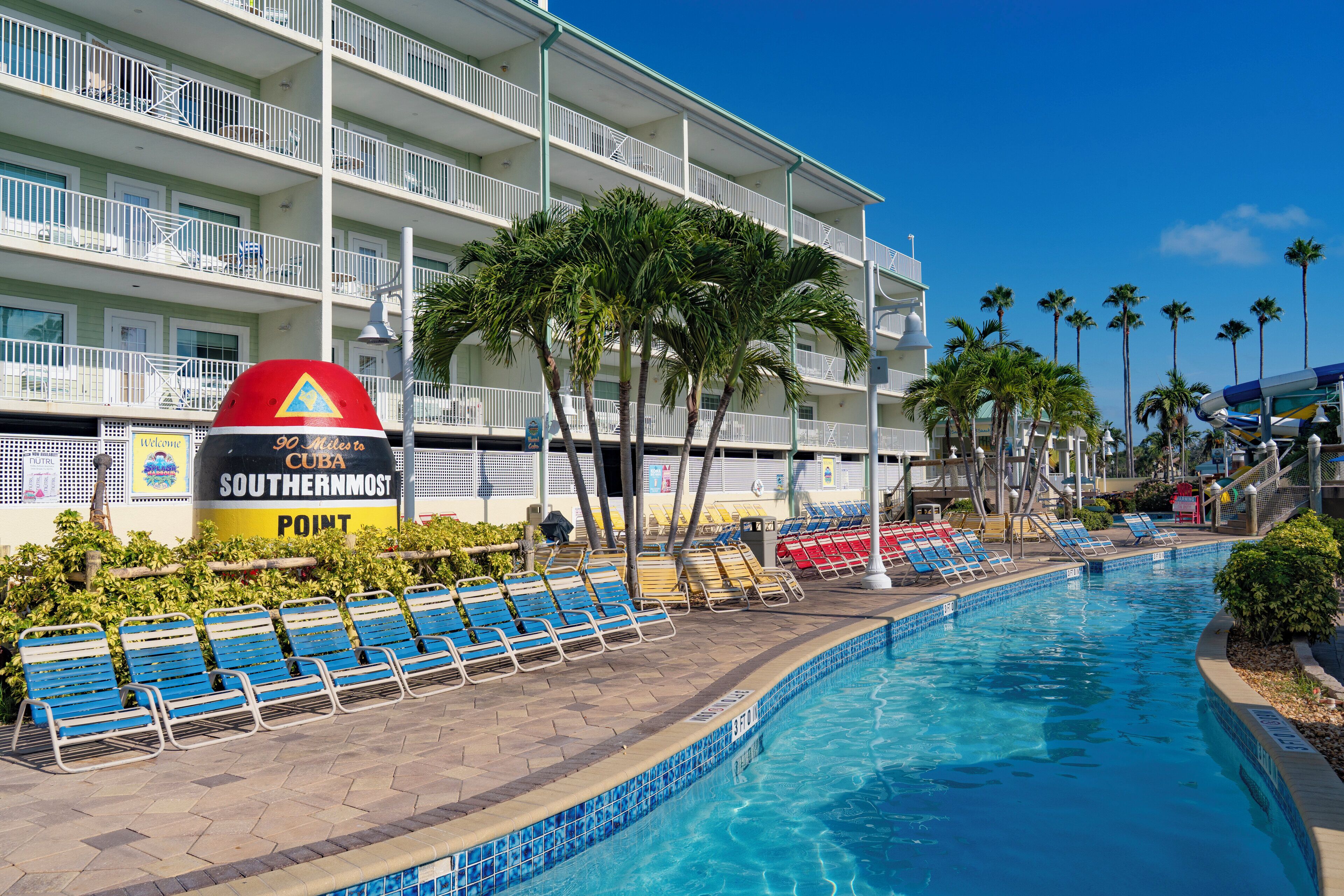 A hotel pool area with a sign indicating '90 Miles to Southernmost Point' and a poolside lounge with sun loungers.