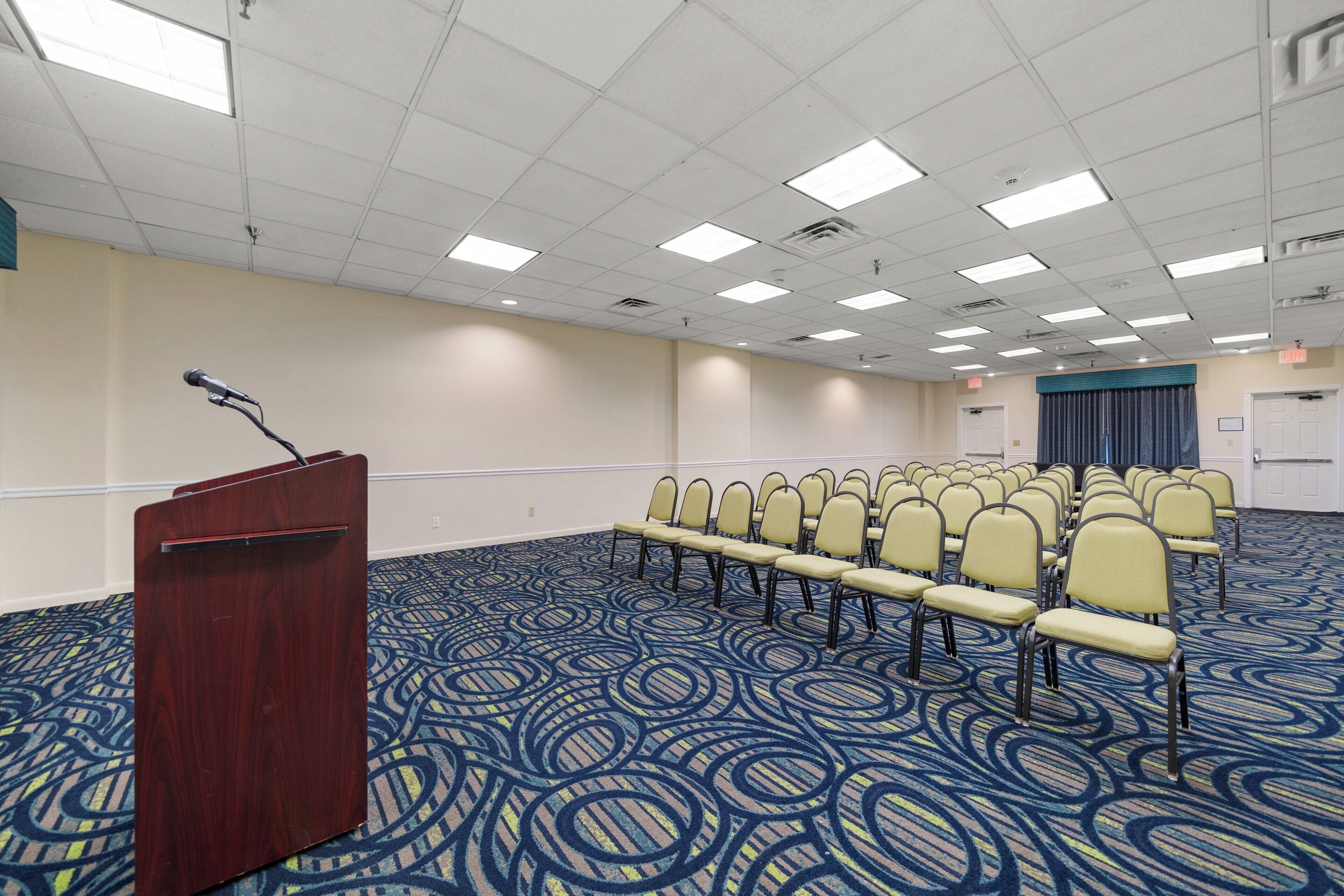 A conference room with a podium, rows of chairs, and a patterned carpet.