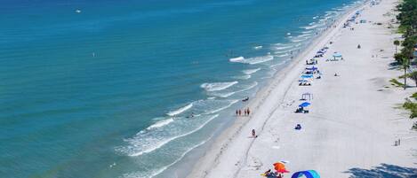 A beach with clear blue water, a sandy shore, and umbrellas.