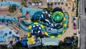 An aerial view of a water park with multiple slides and pools, surrounded by beach areas and lounge chairs. - Holiday Inn & Suites Clearwater Beach S-Harbourside by IHG (Indian Rocks Beach)