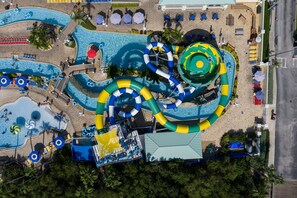Vista aérea de un parque acuático con múltiples toboganes y piscinas, rodeado de zonas de playa y sillones de descanso.