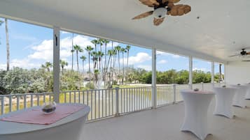 A covered outdoor area with white tables and a view of palm trees and a body of water.