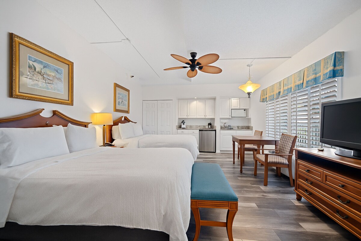 A hotel room with two beds, a dining area, kitchenette, and a TV.