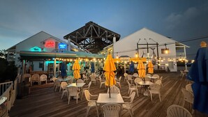 An outdoor dining area with wooden deck and white plastic chairs, featuring a restaurant with neon signs and a covered seating area. - Holiday Inn & Suites Clearwater Beach S-Harbourside by IHG (Indian Rocks Beach)