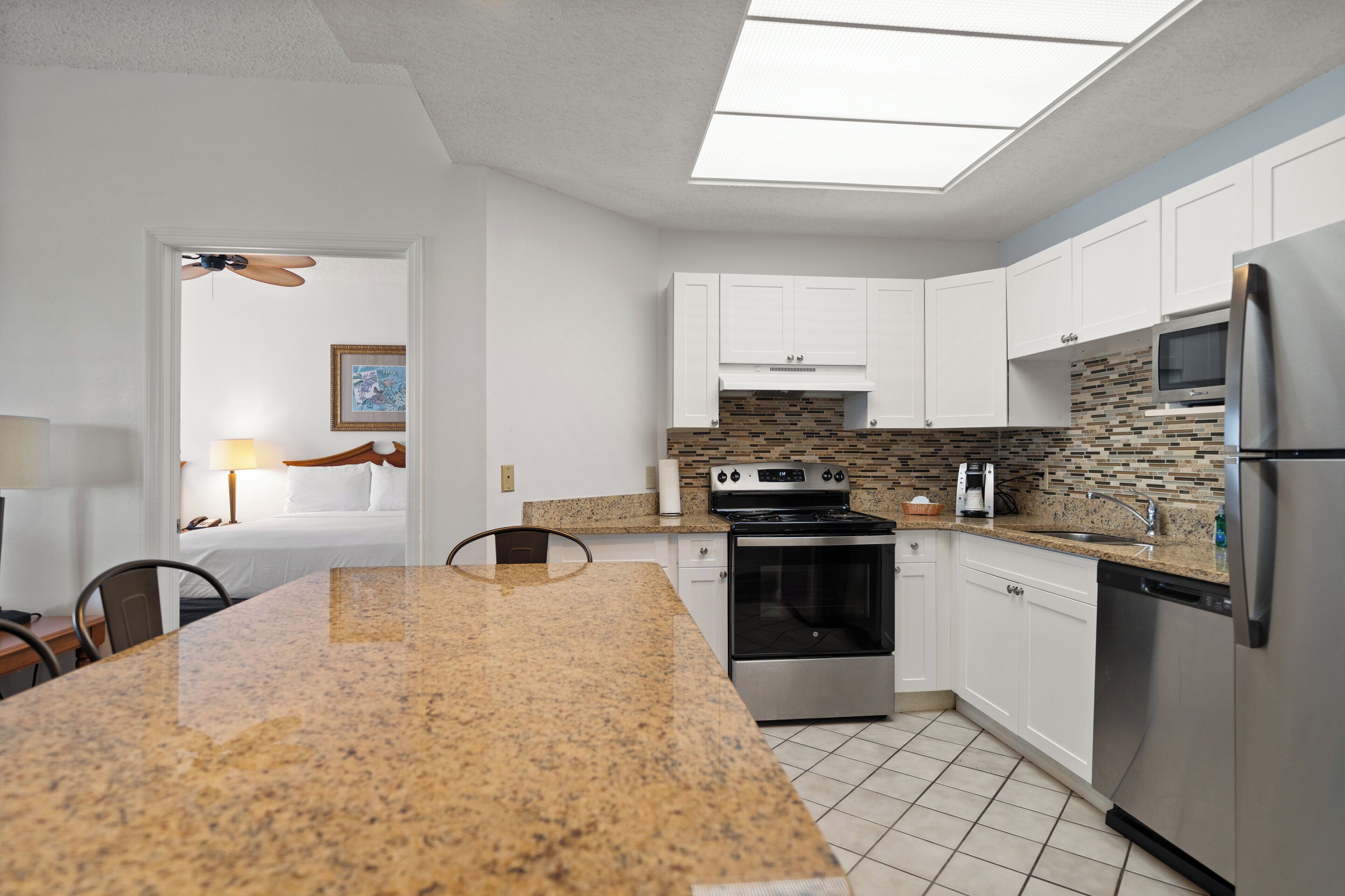 A modern kitchen with white cabinets, a granite countertop, a stainless steel refrigerator, and a built-in oven.