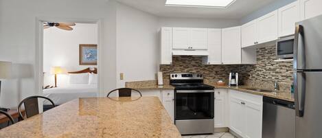 A modern kitchen with white cabinets, a granite countertop, a stainless steel refrigerator, and a built-in oven.