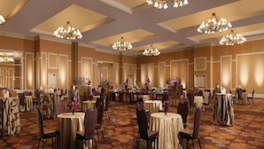 Een feestzaal met ronde tafels, stoelen, kroonluchters en een kamerbreed tapijt met dessin.
