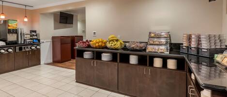 A modern kitchen area with a coffee station, fruit bowls, and storage cabinets.