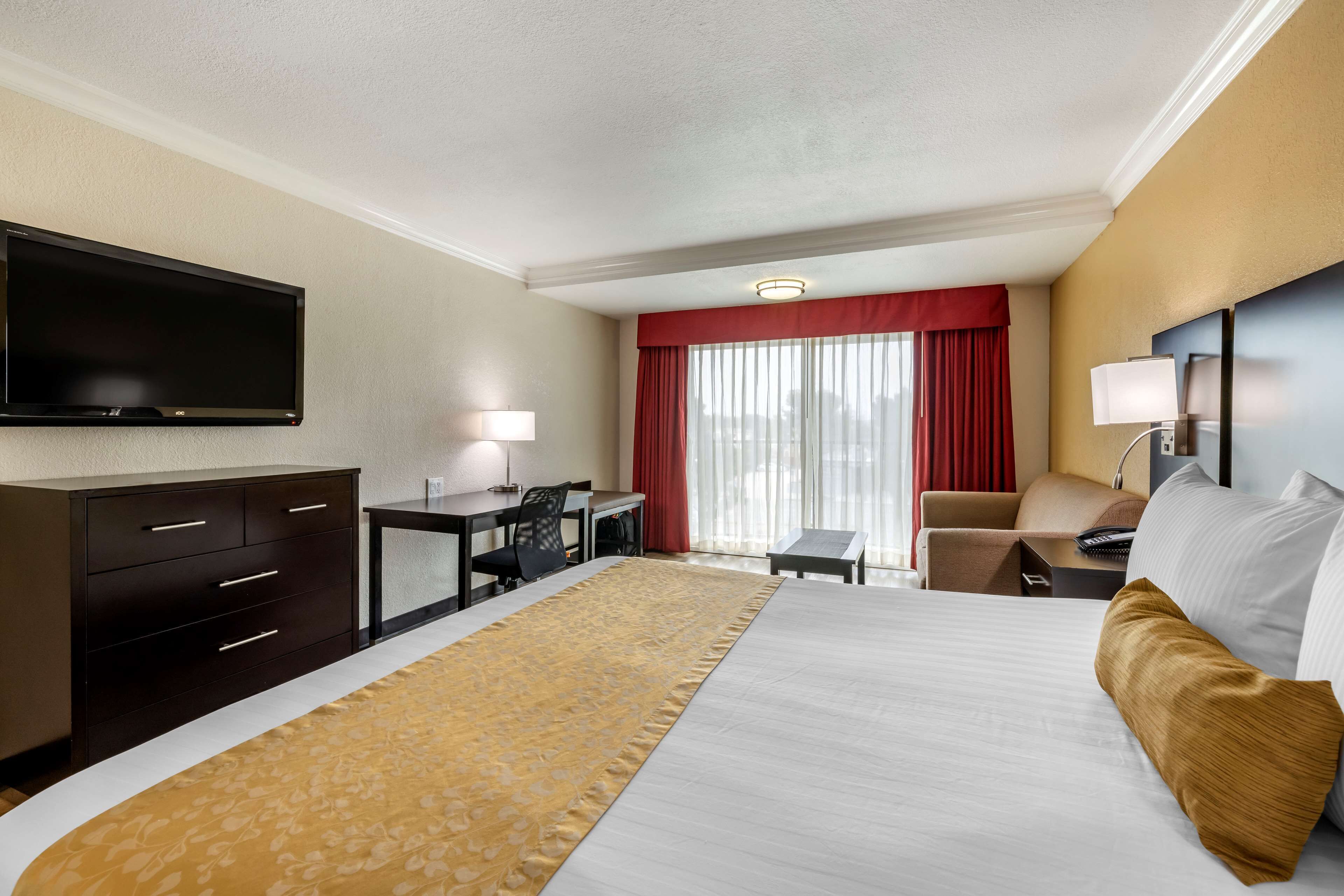 A hotel room with a large bed, a desk, a chair, a TV, and a window with curtains.