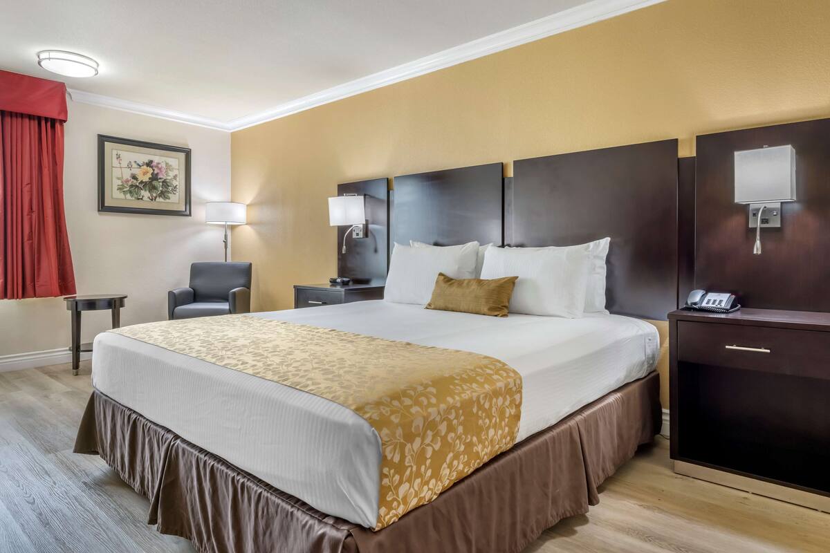 Ett hotellrum med en stor säng, sängbord, ett skrivbord, en stol, en lampa och en telefon.