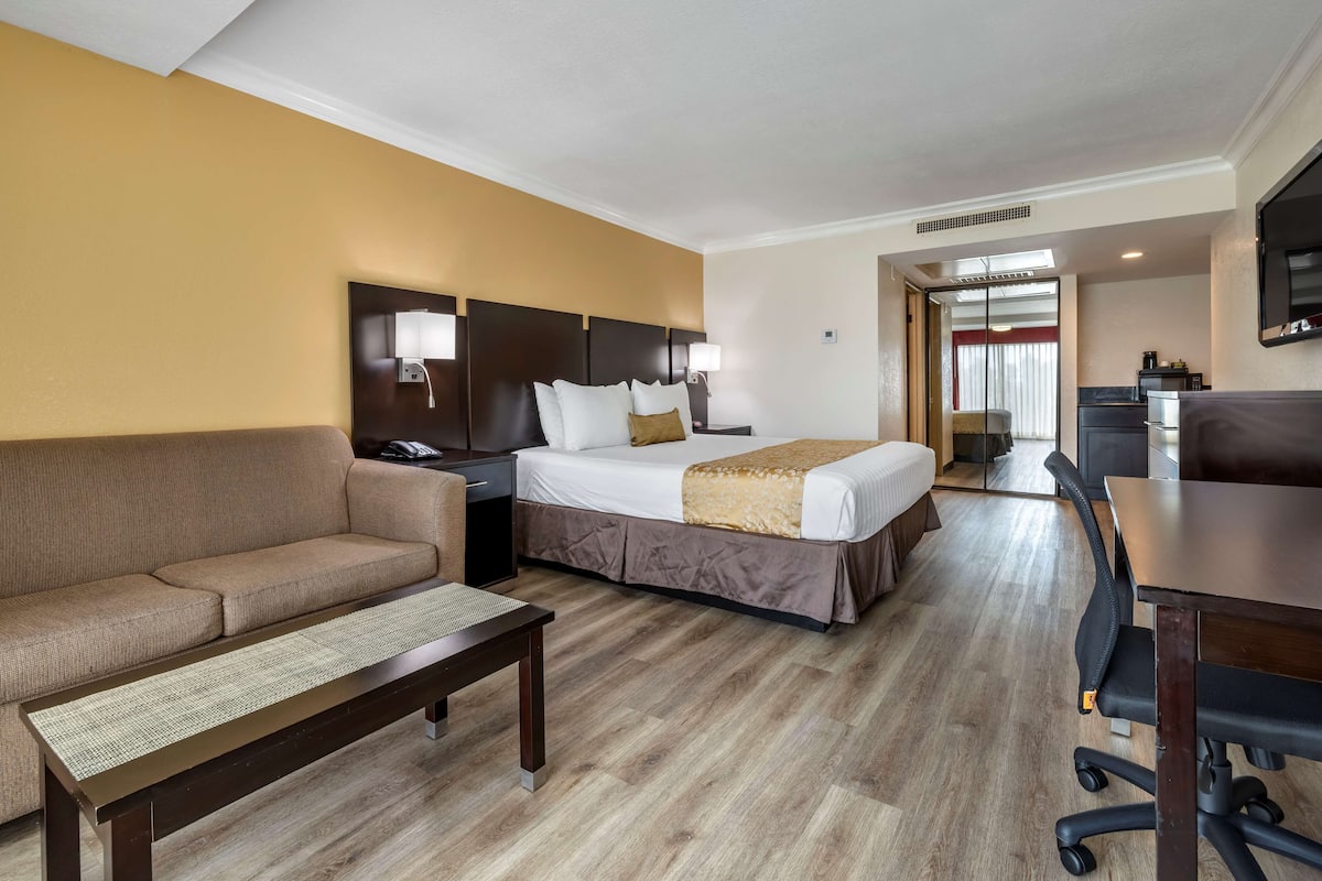 Ett hotellrum med en säng, soffa, skrivbord och ett litet kök.