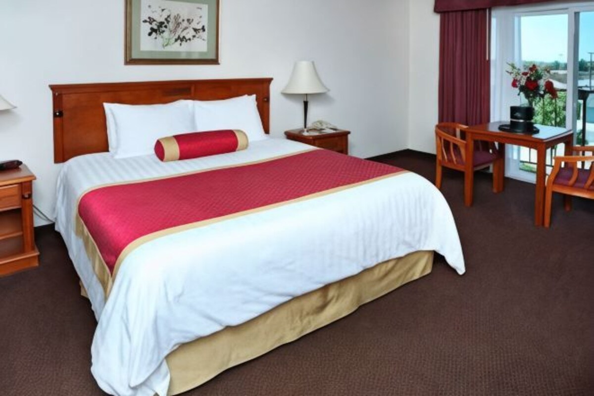 A hotel room with a large bed, a desk, a chair, a nightstand, and a window with a view.