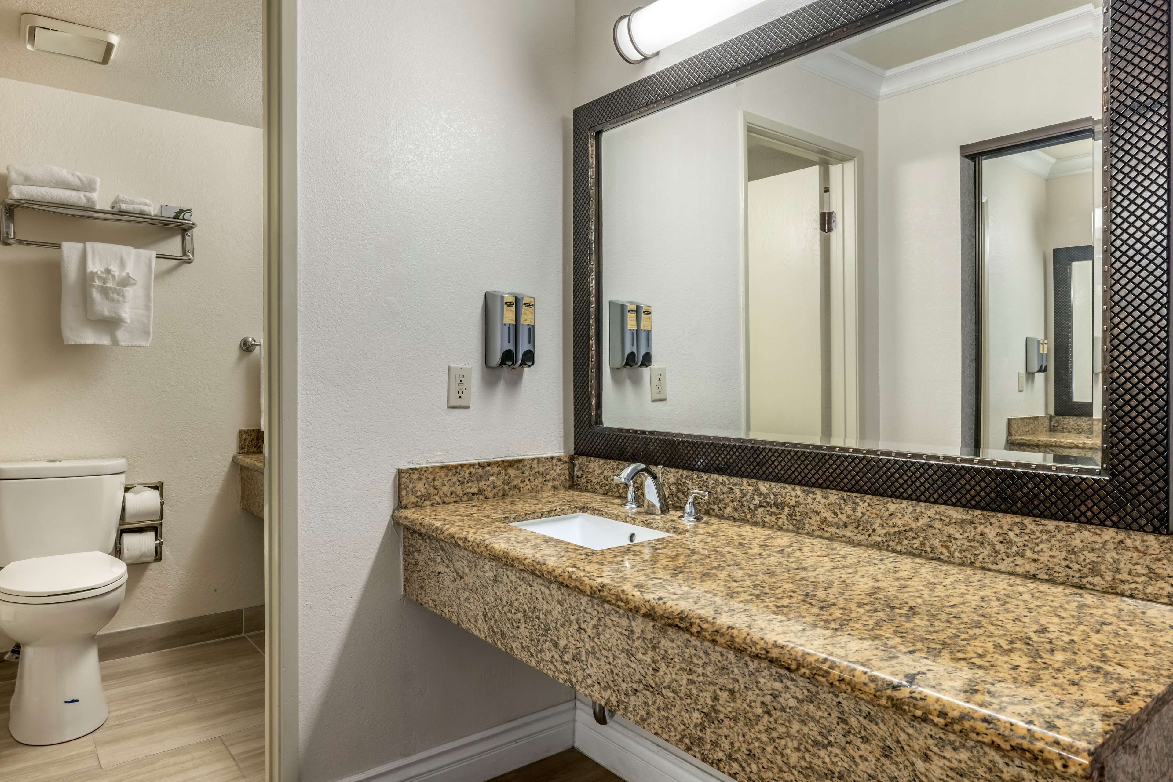 A bathroom with a granite countertop sink, a toilet, and a mirror with a black frame.