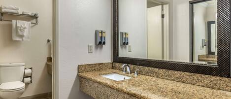 A bathroom with a granite countertop sink, a toilet, and a mirror with a black frame.