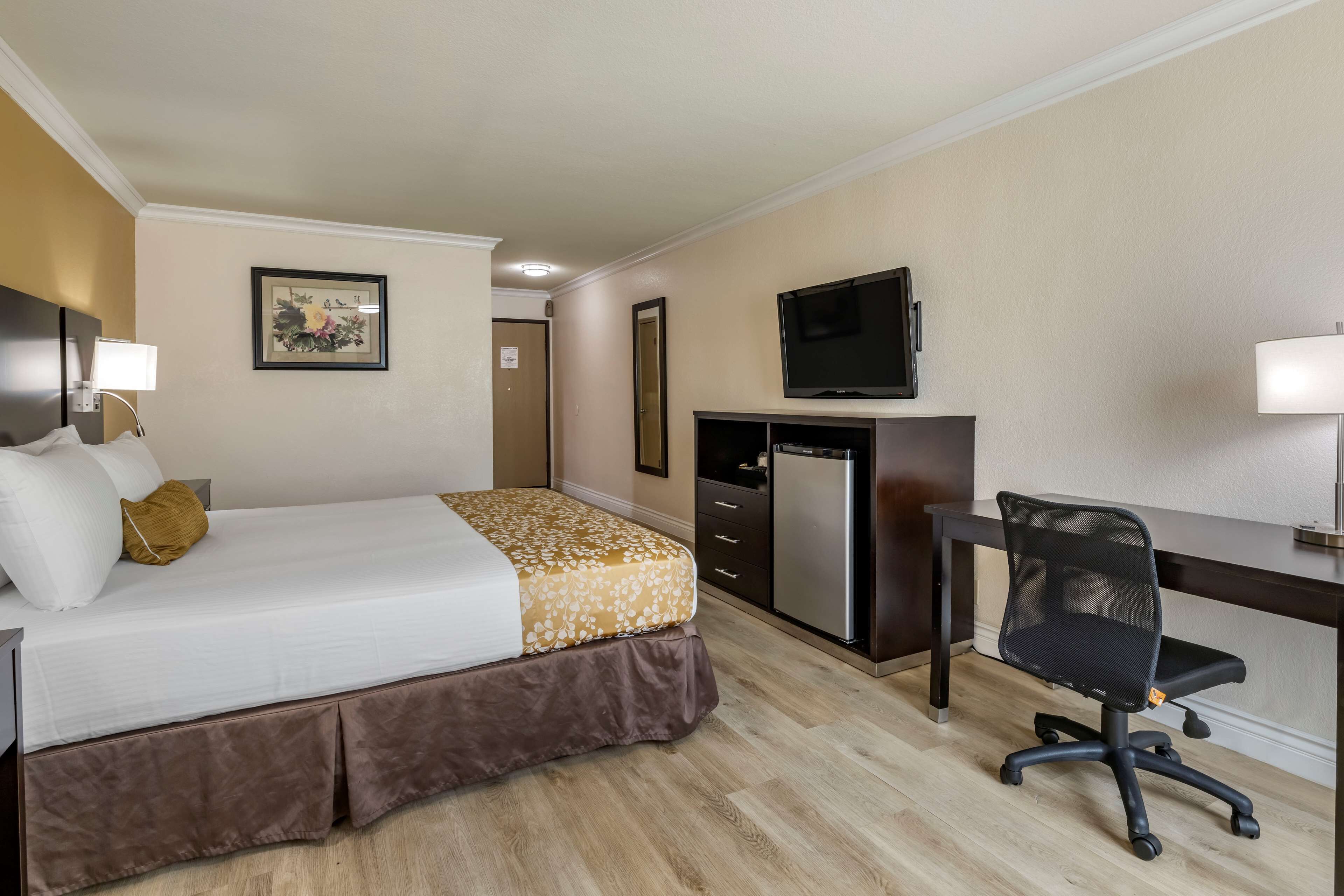 Ein Hotelzimmer mit Bett, Schreibtisch, Stuhl, Fernseher und kleinem Kühlschrank.