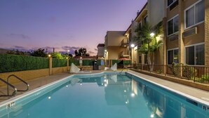 Uma piscina com água azul cristalina, cercada por um muro de tijolos e um hedge.